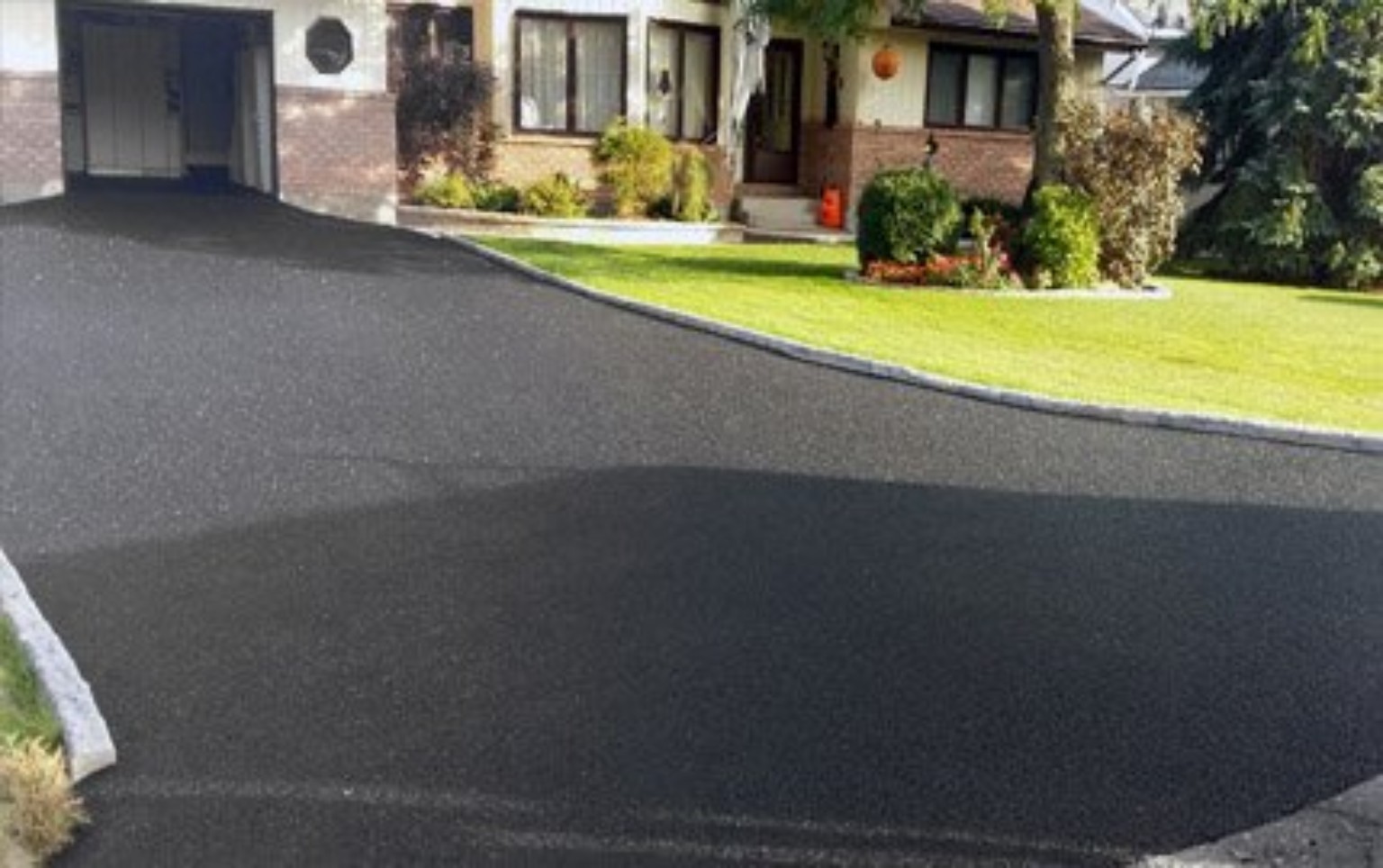 Fresh black tarmac driveway around landscaped garden